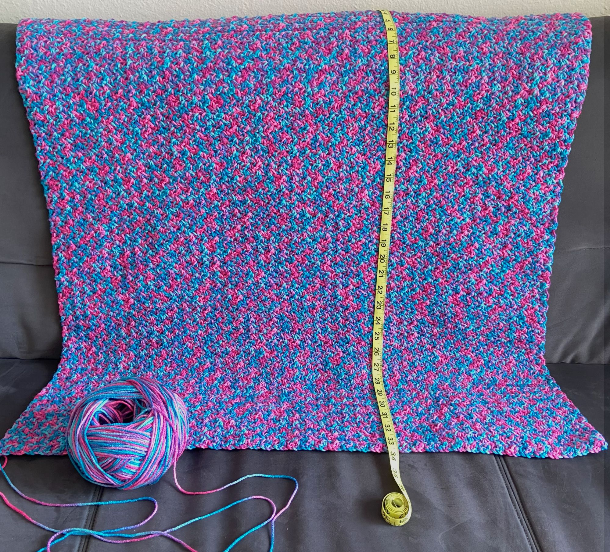 a multicolored crochet blanket draped on a couch with measuring tape